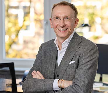 Einzelfoto von Christian Müller in Business-Kleidung mit verschränkten Armen und lächelndem Blick in die Kamera.